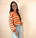 Person wearing an orange and white striped sweater with light blue jeans on a beige background