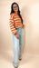 Woman wearing an orange and white striped sweater and light blue jeans against a beige background