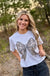 A woman wearing a gray t-shirt with a camo bow design, standing outdoors.